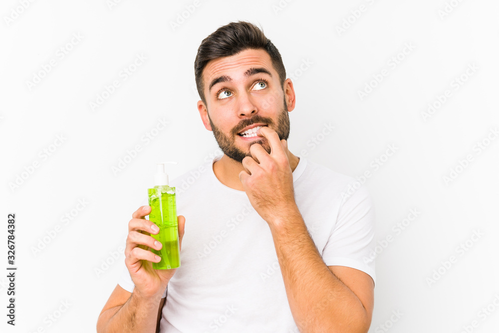 Young caucasian man holding a moisturizer with aloe vera isolated relaxed thinking about something looking at a copy space. Young caucasian man holding a moisturizer with aloe vera isolated relaxed thinking about something looking at a copy space.