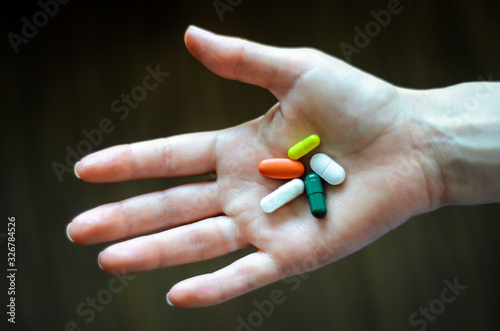 Open female thenar holding two white, red, green, yellow pills, on a dark background