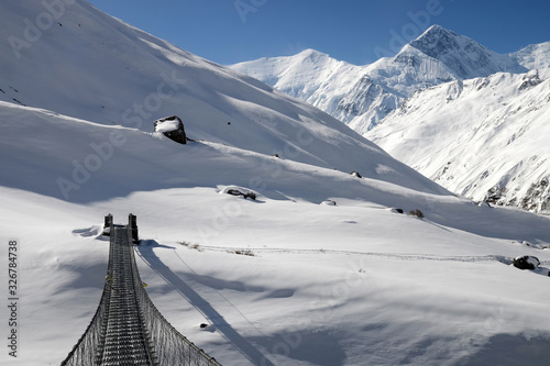 Iron bridge on Annapurna Circuit trek. Anapurna III Peak (7 555 m) and Gangapurna Peak (7 455 m) on the background..