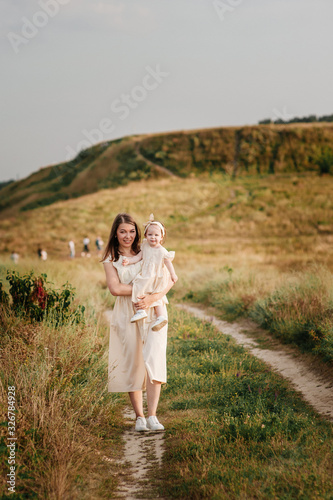 Family, mom, daughter are walking on a hill in the field in yellow identical dresses. © malysheva