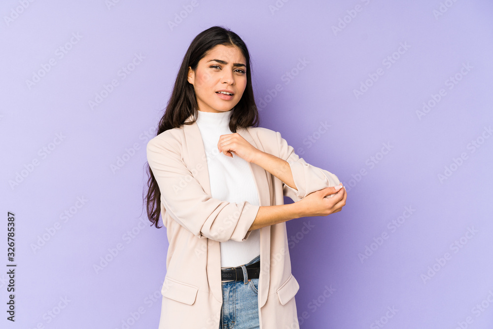 Young indian woman isolated on purple background massaging elbow, suffering after a bad movement. Young indian woman isolated on purple background massaging elbow, suffering after a bad movement.