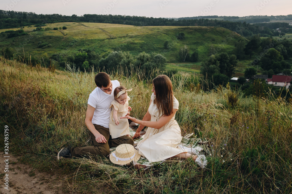Family, mom, dad, daughter on picnic on a hill in the field. Mom and daughter in yellow identical dresses. Family, mom, dad, daughter on picnic on a hill in the field. Mom and daughter in yellow identical dresses.