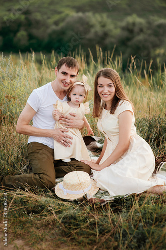 Family, mom, dad, daughter on picnic on a hill in the field. Mom and daughter in yellow identical dresses.
