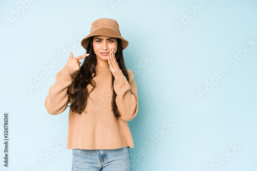 Young indian woman wearing a hat isolated on blue background having a strong teeth pain, molar ache.