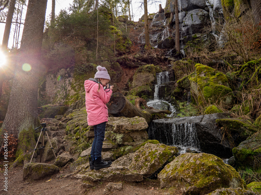 A girl takes pictures of forest landscapes. Girl at the waterfall.