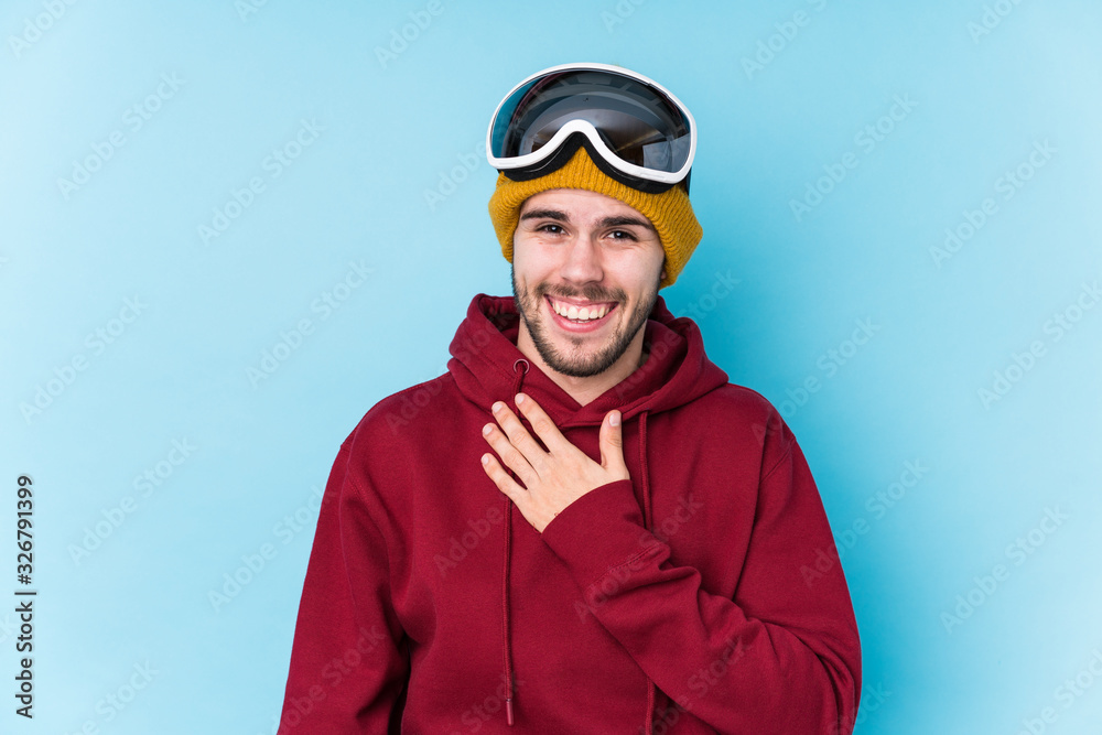 Young caucasian man wearing a ski clothes isolated laughs out loudly keeping hand on chest. Young caucasian man wearing a ski clothes isolated laughs out loudly keeping hand on chest.
