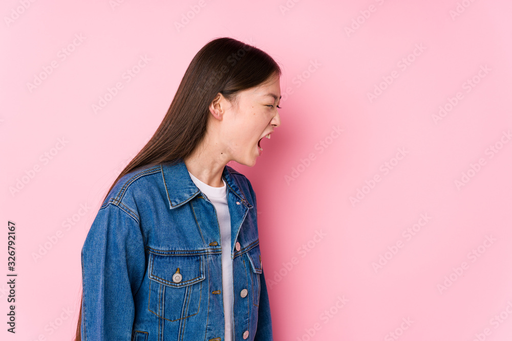 Young chinese woman posing in a pink background isolated shouting towards a copy space
