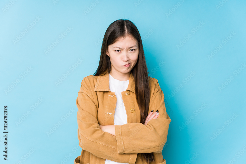 Young chinese woman posing in a blue background isolated frowning face in displeasure, keeps arms folded. Young chinese woman posing in a blue background isolated frowning face in displeasure, keeps arms folded.