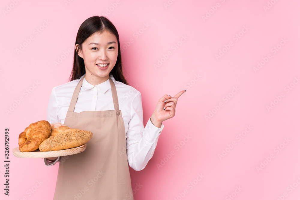 Young chinese baker woman isolated smiling and pointing aside, showing something at blank space.
