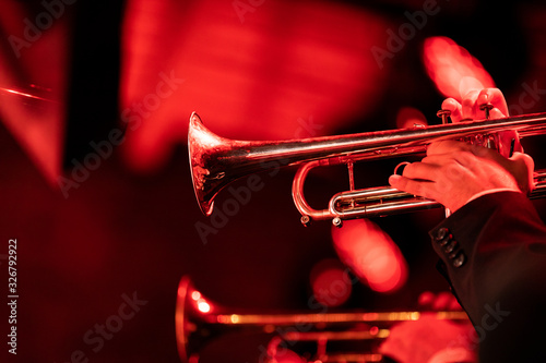 Two trumpet players playing their instrument in the trumpet section of a big band during a concert with red stage lights