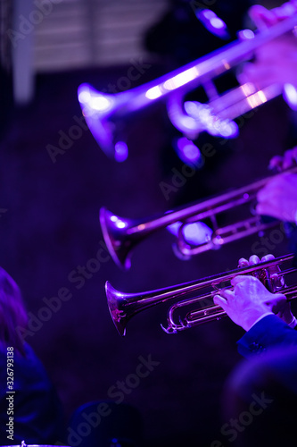  The trumpet section of a big band is playing a chorus during a concert on stage in purple stage lights