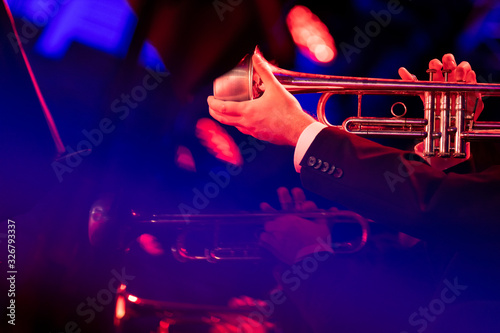 A trumpet player of a trumpet big band section is playing with a mute while holding in during a live performance of a jazz concert in a venue with red and blue lights