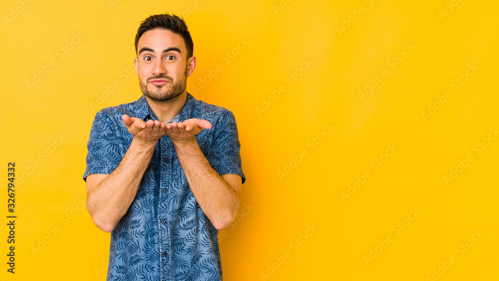 Young caucasian man isolated on yellow bakground folding lips and holding palms to send air kiss. Young caucasian man isolated on yellow bakground folding lips and holding palms to send air kiss.