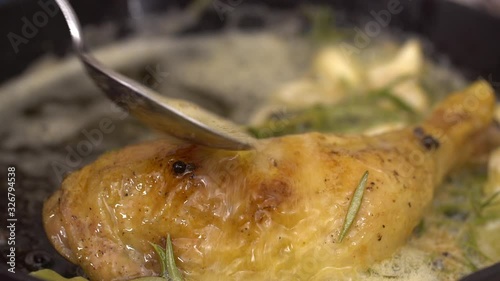 Chef pouring chicken leg with melted butter mixture with thyme, bay leaf and pepper, close up view