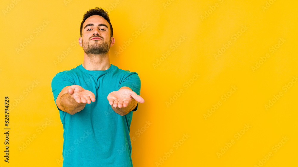 Young caucasian man isolated on yellow bakground folding lips and holding palms to send air kiss. Young caucasian man isolated on yellow bakground folding lips and holding palms to send air kiss.