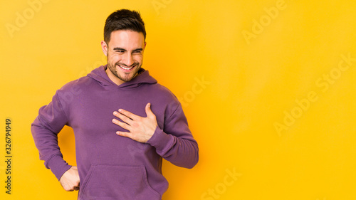 Young caucasian man isolated on yellow bakground laughing keeping hands on heart, concept of happiness.