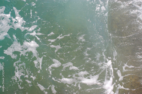 Top view texture waves, foaming and splashing in the ocean, sunny day. Beautiful tropical sea in summer season image by aerial view. Abstract sea background. Ocean waves close-up.