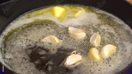 Female chef is putting garlic on pan, close up shot of iron pan on gas stove with big chunks of butter melting on grill surface.	