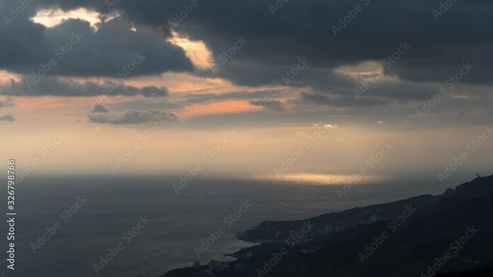 Sunset over the sea. Flying dark clouds with sunbeams over glittering sea surface near the rocky coasts at twilight, time lapse Sunset over the sea. Flying dark clouds with sunbeams over glittering sea surface near the rocky coasts at twilight, time lapse