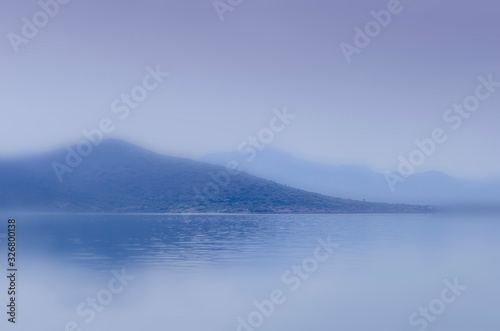 An abstract blurry blue seascape with two mountain rages and water foreground suitable as background with plenty of copy space. 