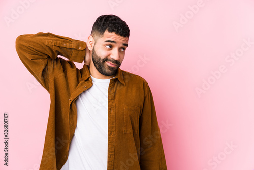 Young latin man against a pink background isolated touching back of head, thinking and making a choice. photo