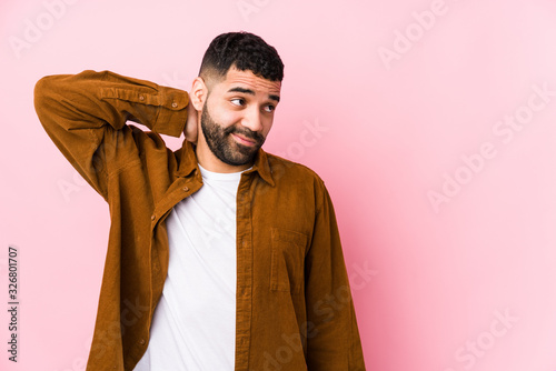 Young latin man against a pink background isolated touching back of head, thinking and making a choice.
