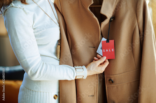 Closeup on woman examines sale price tag on beige coat