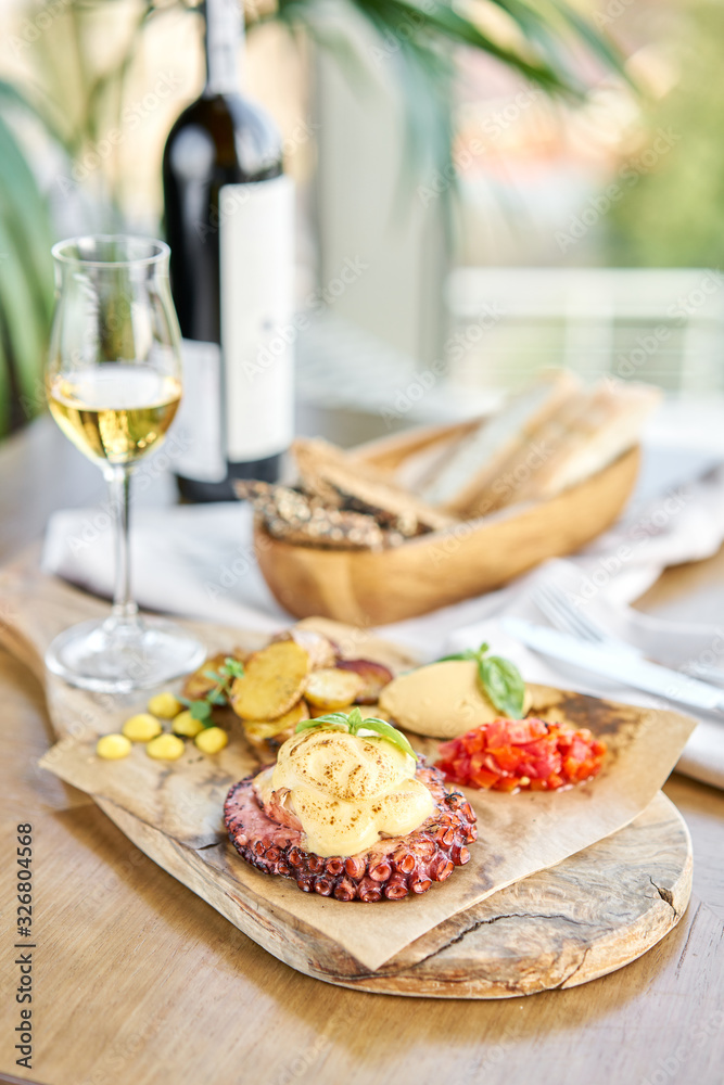 Roasted octopus BBQ and Baked potato with a glass of Grapa. Wooden plate. Restaurant menu Roasted octopus BBQ and Baked potato with a glass of Grapa. Wooden plate. Restaurant menu