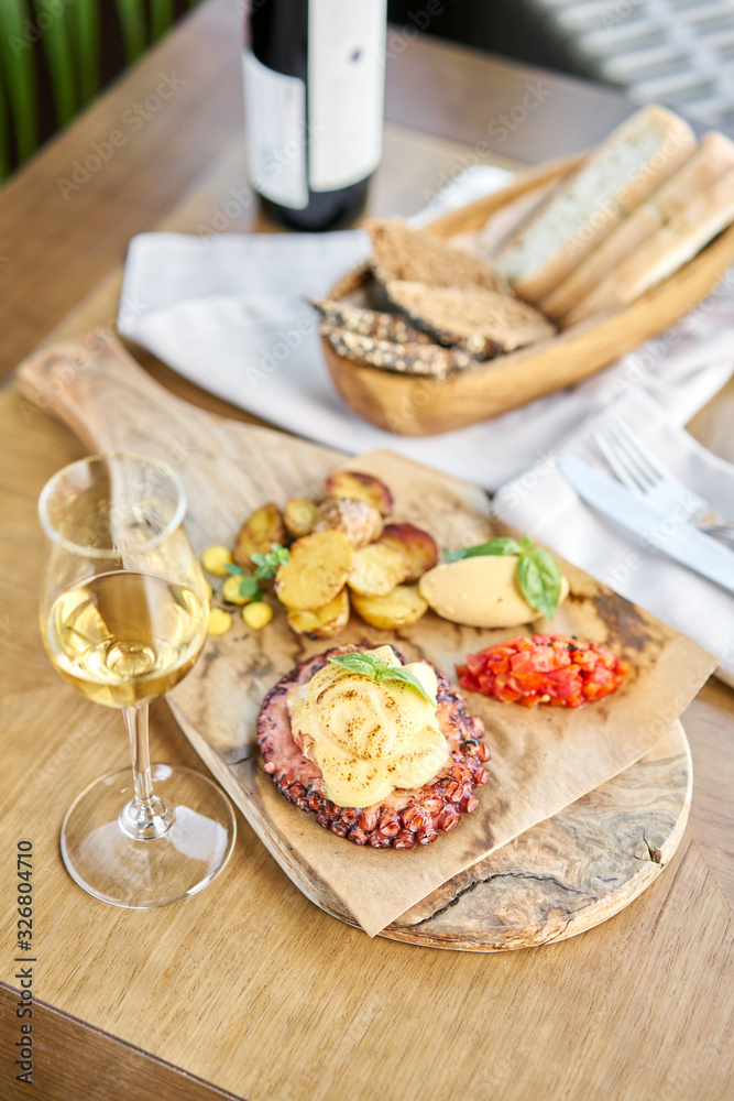Roasted octopus BBQ and Baked potato with a glass of Grapa. Wooden plate. Restaurant menu Roasted octopus BBQ and Baked potato with a glass of Grapa. Wooden plate. Restaurant menu