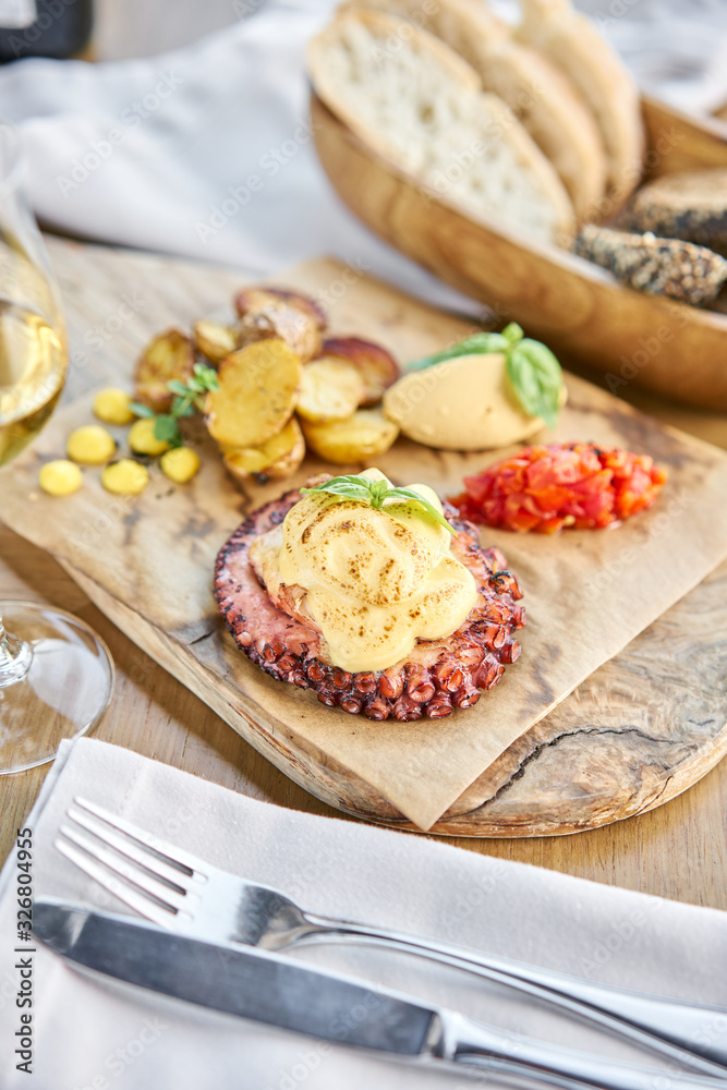 Roasted octopus BBQ and Baked potato with a glass of Grapa. Wooden plate. Restaurant menu