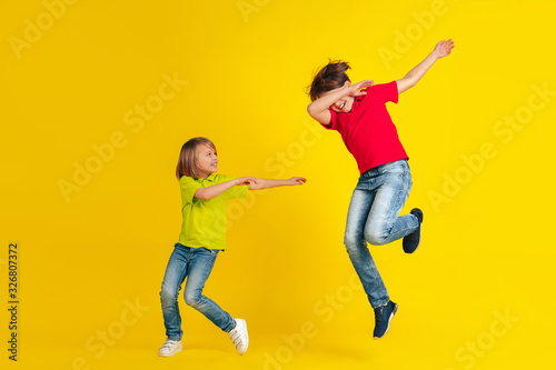 Winner. Happy children playing and having fun together on yellow studio background. Caucasian kids in bright clothes looks playful, laughting, smiling. Concept of education, childhood, emotions.