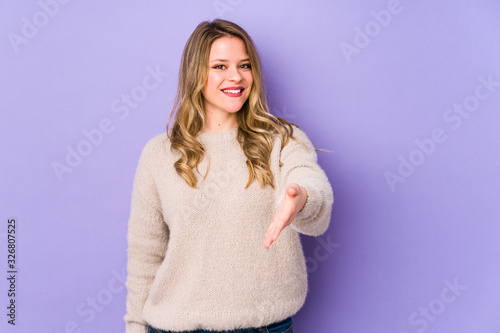 Young caucasian woman isolated on purple background stretching hand at camera in greeting gesture.