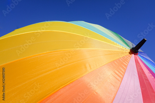 Colorful umbrella protects from the sun a summer day, blue sky background.