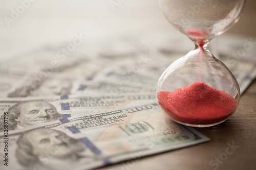 Deadline and time is money concept with hourglass and hundred dollars US Bills currency. Red sandglass. Bear market countdown. currency depreciation.
