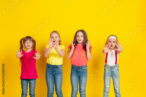 Disguasted. Happy children playing and having fun together on yellow studio background. Caucasian kids in bright clothes looks playful, laughting, smiling. Concept of education, childhood, emotions.