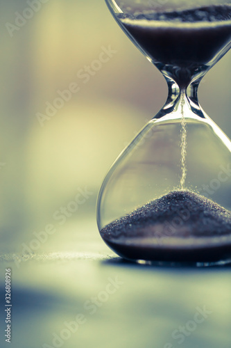 Sand running through the bulbs of an hourglass measuring the passing time in a countdown to a deadline, on a bright background with copy space.