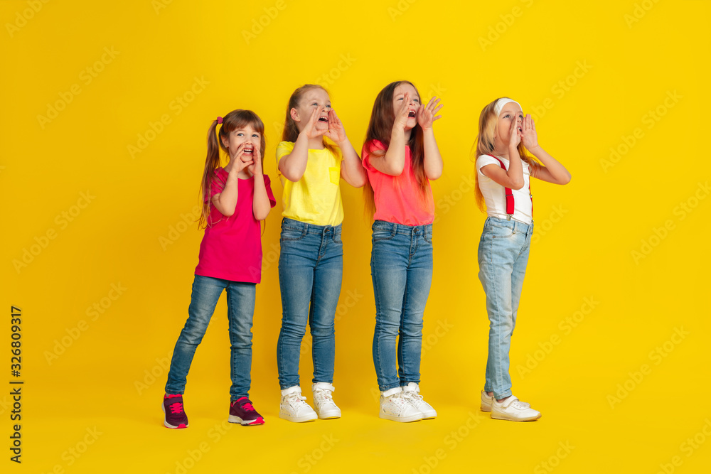 Fototapeta premium Calling. Happy children playing and having fun together on yellow studio background. Caucasian kids in bright clothes looks playful, laughting, smiling. Concept of education, childhood, emotions.