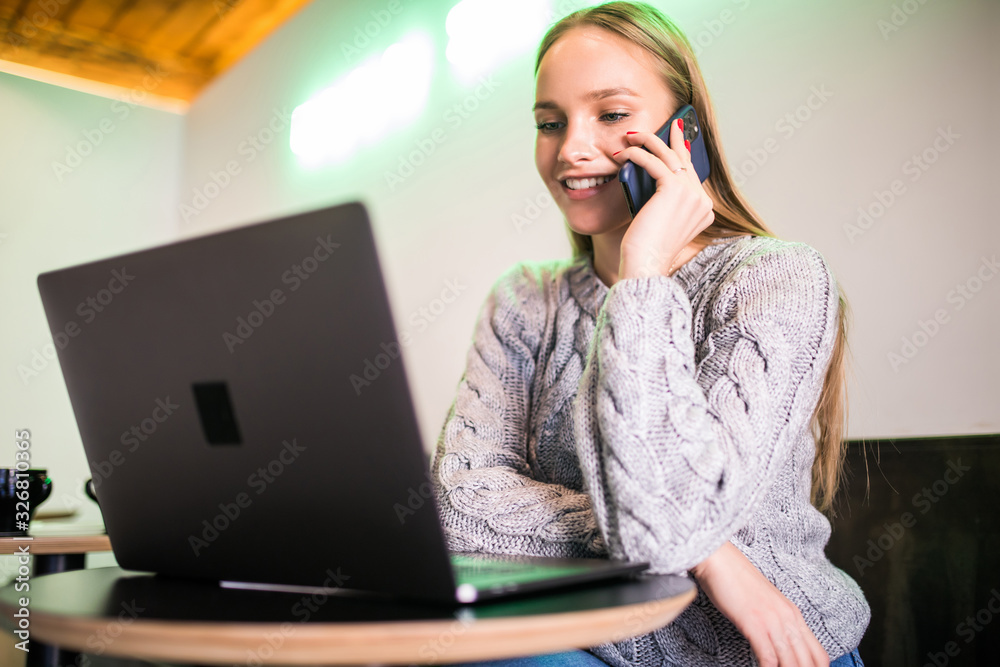 Beautiful young woman using laptop while talking on the phone in cafe Beautiful young woman using laptop while talking on the phone in cafe