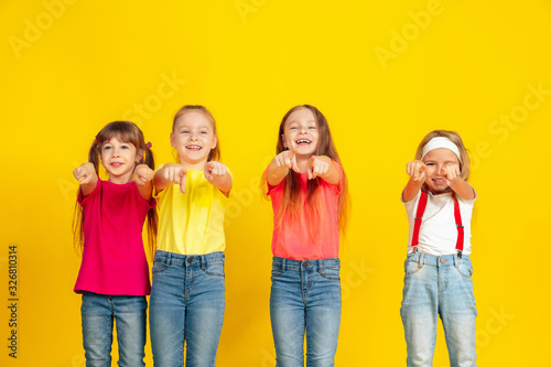 Pointing. Happy children playing and having fun together on yellow studio background. Caucasian kids in bright clothes looks playful, laughting, smiling. Concept of education, childhood, emotions.
