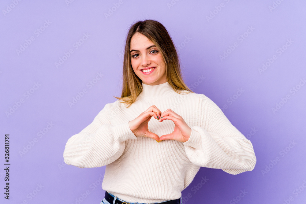 Young caucasian woman isolated on purple background smiling and showing a heart shape with hands. Young caucasian woman isolated on purple background smiling and showing a heart shape with hands.