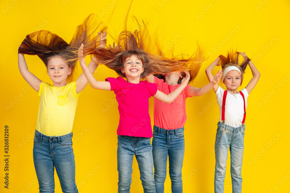 Dancing. Happy children playing and having fun together on yellow studio background. Caucasian kids in bright clothes looks playful, laughting, smiling. Concept of education, childhood, emotions.