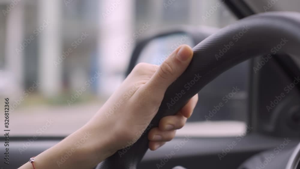 Woman hand holding steering wheel, driving car in city traffic Woman hand holding steering wheel, driving car in city traffic