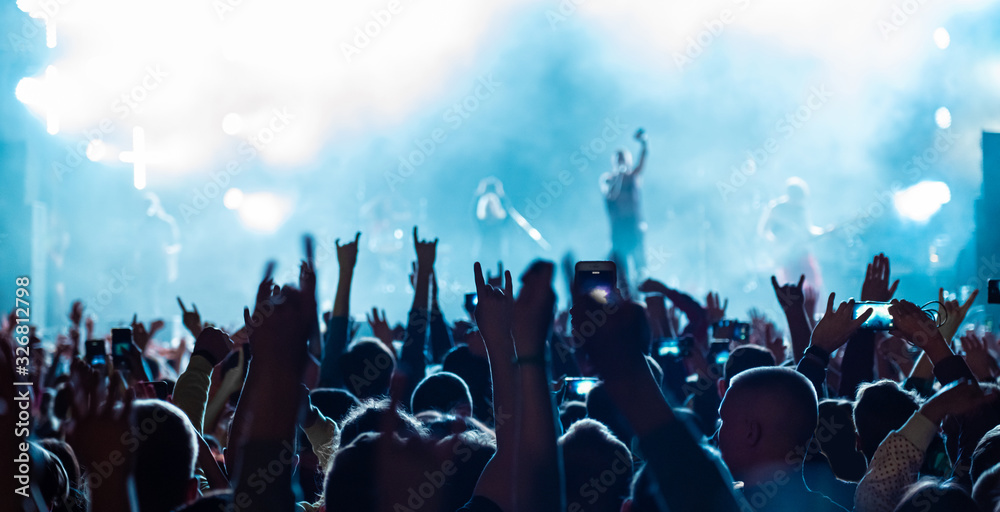 Rear back view of audience crowd people fans raising hands enjoying live  music festival concert event concept shooting on phones rock band  silhouettes performance sing on night club outdoor stage. Stock Photo