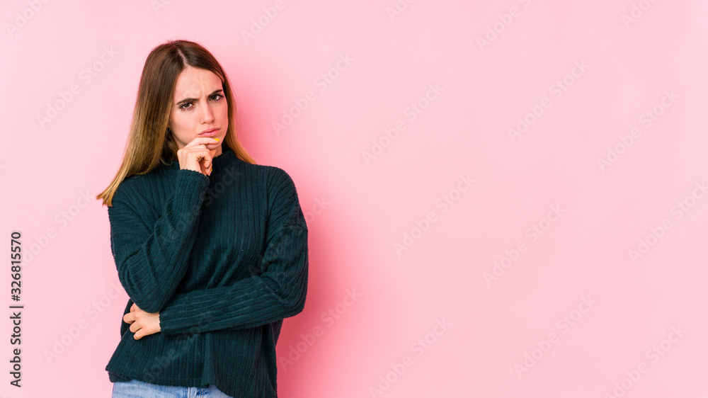 Young caucasian woman isolated on pink background thinking and looking up, being reflective, contemplating, having a fantasy.
