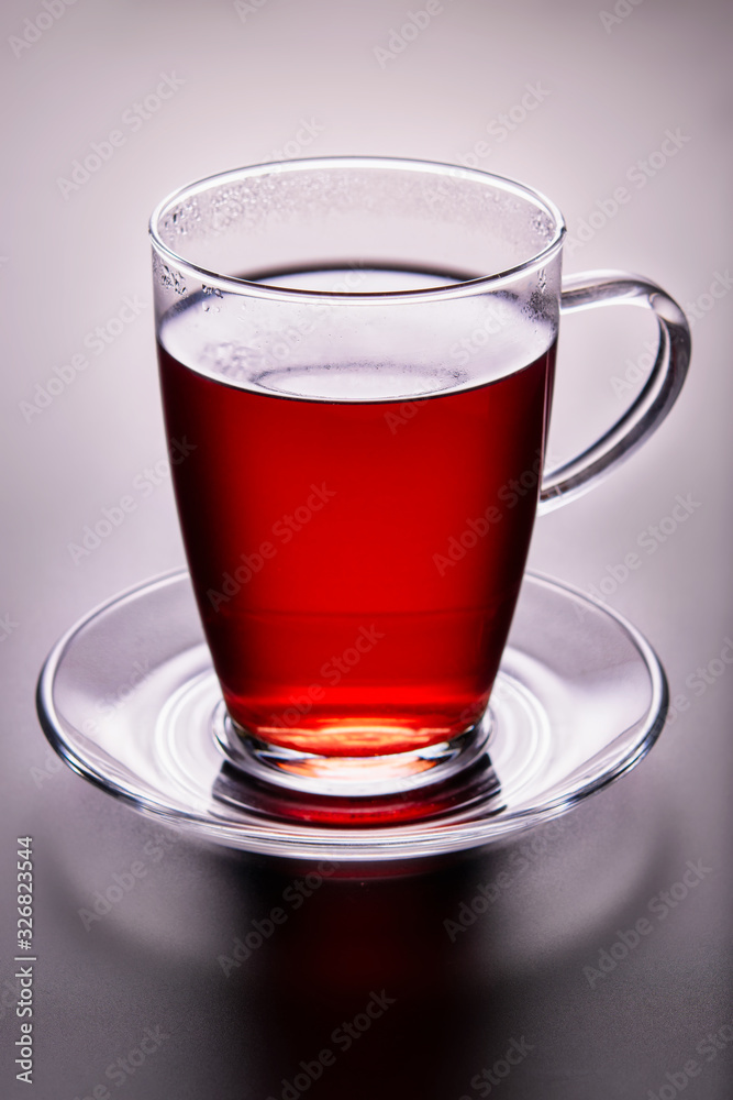 Close-up of tea glass with red fruit tea, on a glass saucer. Backlight illuminated. Close-up of tea glass with red fruit tea, on a glass saucer. Backlight illuminated.