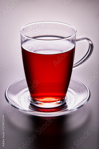 Close-up of tea glass with red fruit tea, on a glass saucer. Backlight illuminated.