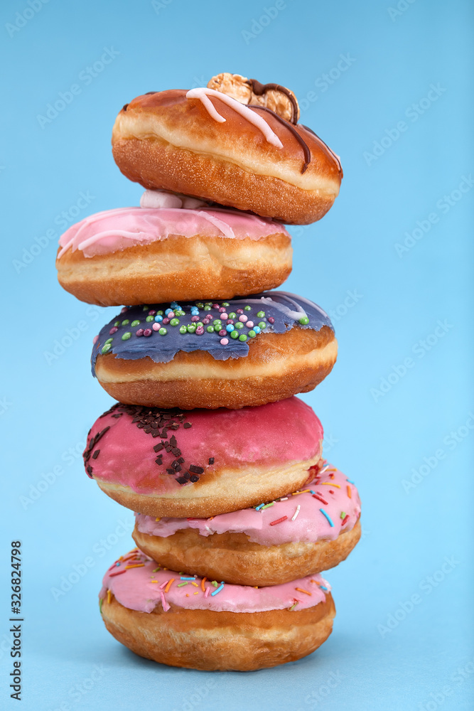 A stack of sweet donuts on a blue background. Concept desserts, different colored donuts laid out on top of each other by a tower. Copy space, blue background.