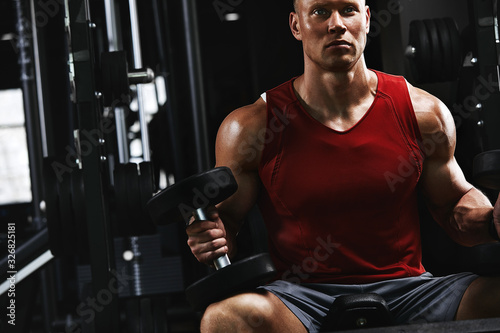 Young sports athlete fitness model, in the sports hall shakes biceps dumbbells portrait shot. Close-up Sports motivation, low key, high contrast. The concept of a healthy lifestyle, life movement