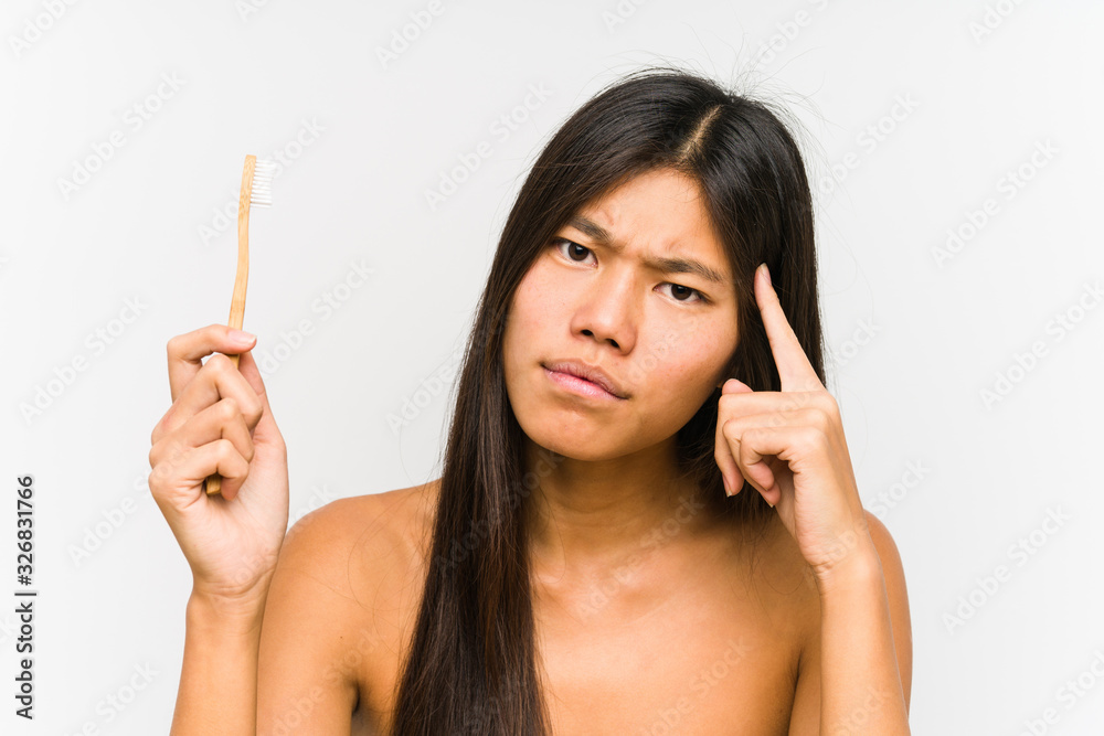 Young chinese woman holding a teeth brush isolated pointing his temple with finger, thinking, focused on a task. Young chinese woman holding a teeth brush isolated pointing his temple with finger, thinking, focused on a task.