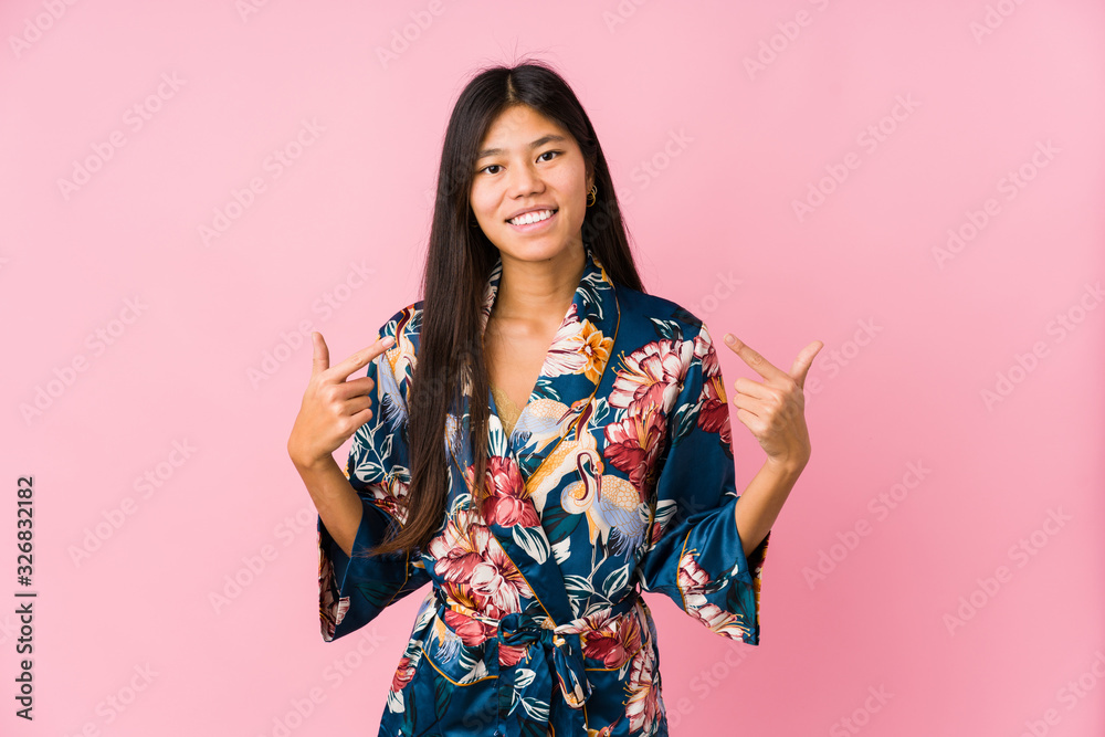Young asian woman wearing a kimono pajamas smiles, pointing fingers at mouth. Young asian woman wearing a kimono pajamas smiles, pointing fingers at mouth.